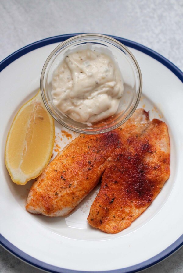air fryer tilapia with tartar sauce and a lemon wedge.