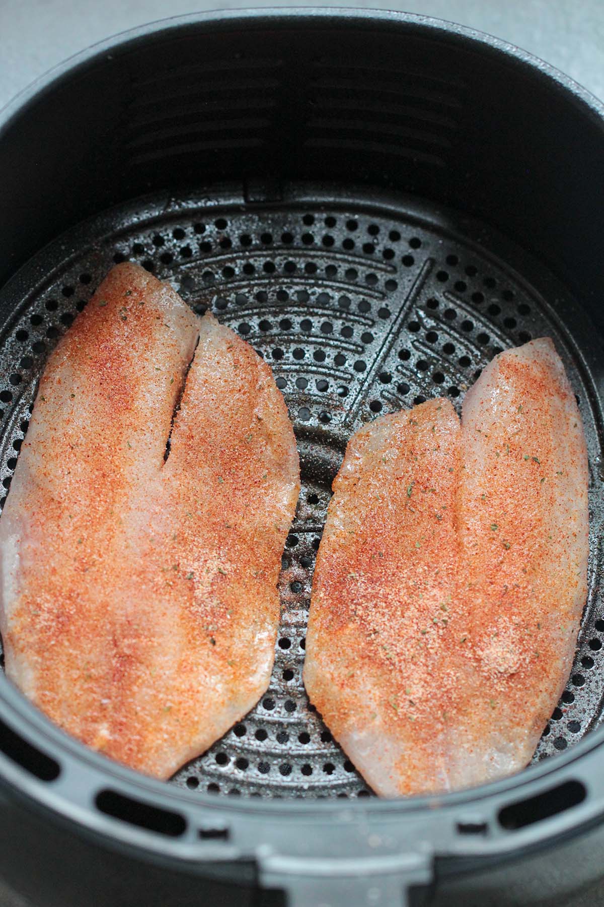 two tilapia fillets in the air fryer basket. 