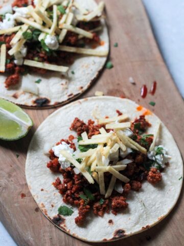 two chorizo tacos on a wooden board.