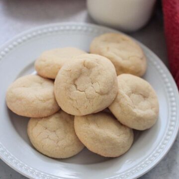 sugar cookies on a white plate with a red towel and milk in the background.