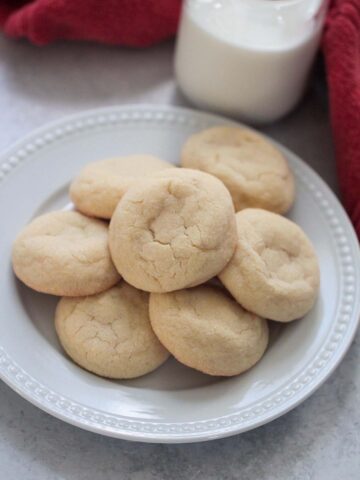 sugar cookies on a white plate with a red towel and milk in the background.