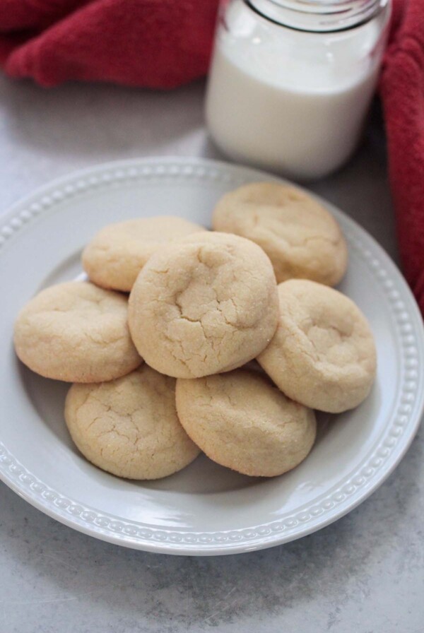 sugar cookies on a white plate with a red towel and milk in the background.