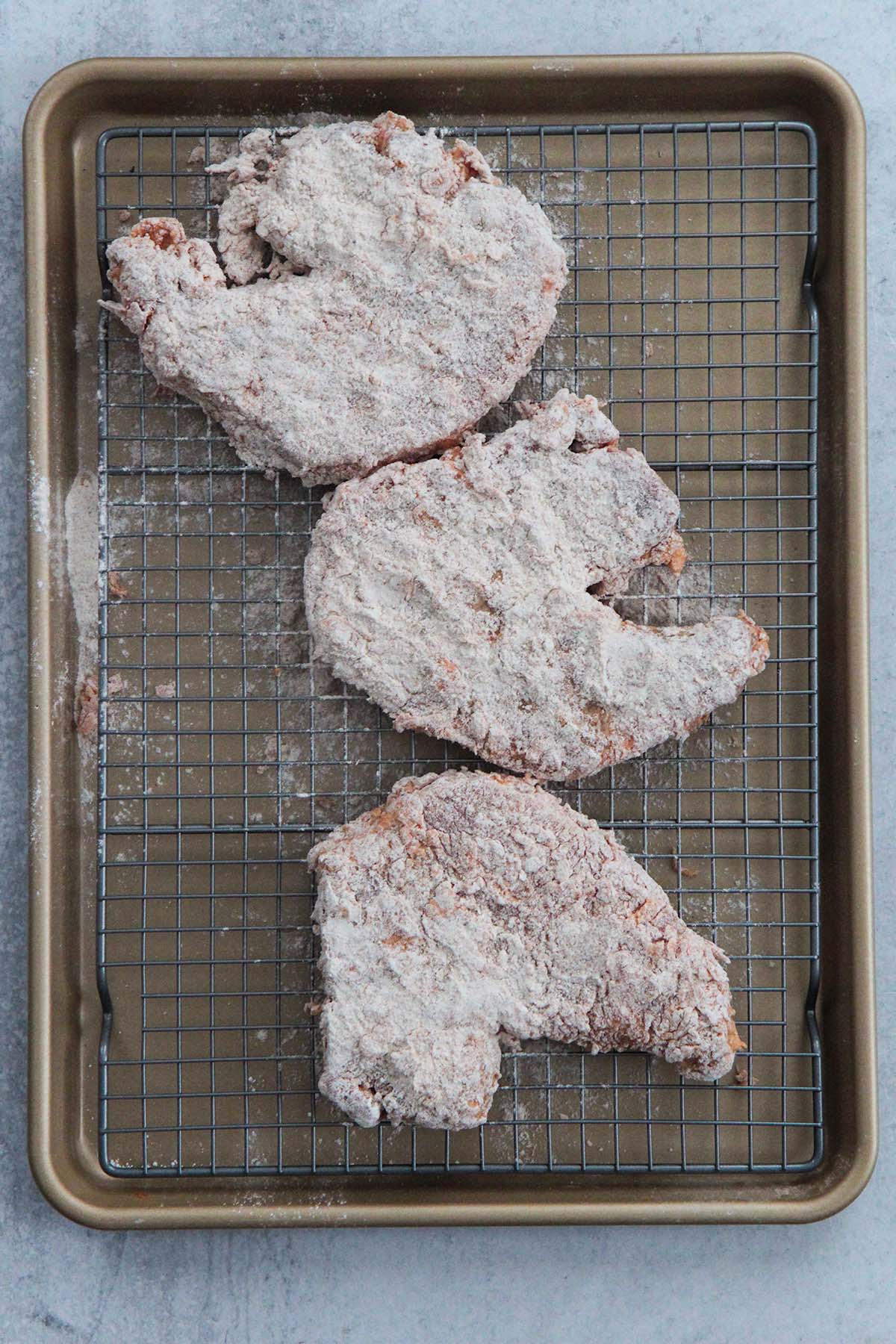 three flour coated bone-in pork chops on a wire rack. 