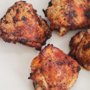 four air fryer chicken thighs on a white plate.