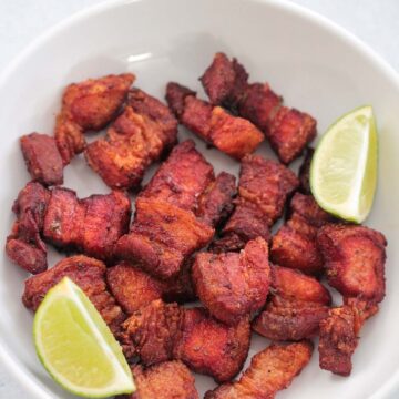 air fryer pork belly in a white plate with two lime wedges.