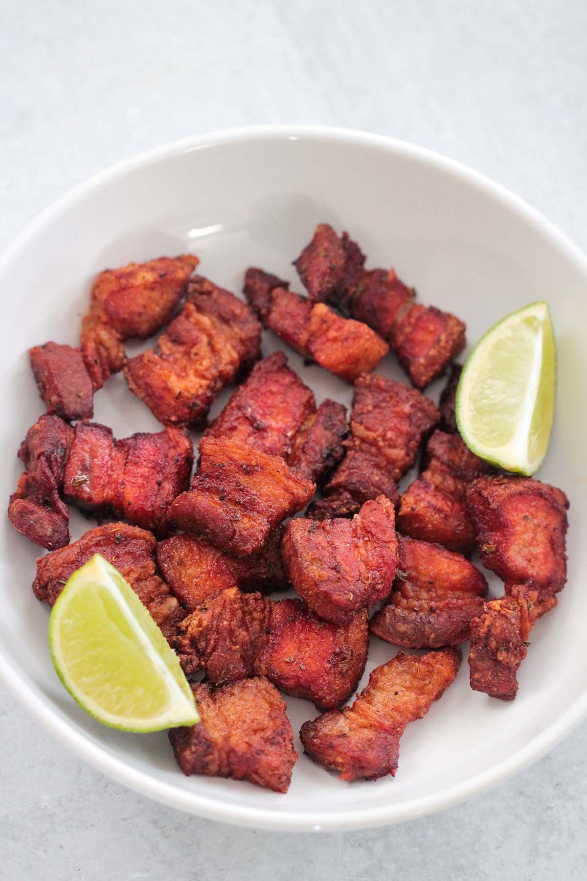air fryer pork belly in a white plate with two lime wedges. 