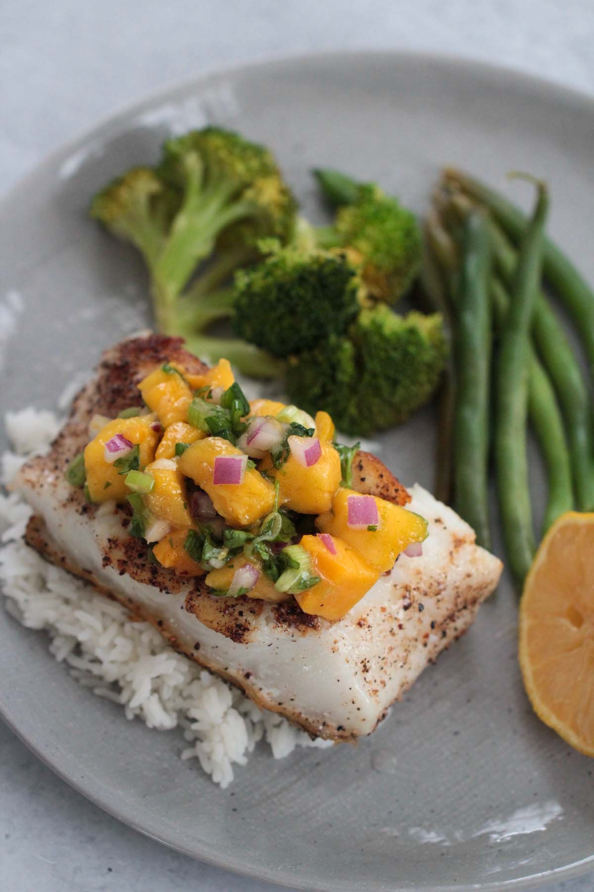 white fish with broccoli, mango salsa, green beans, and a lemon. 