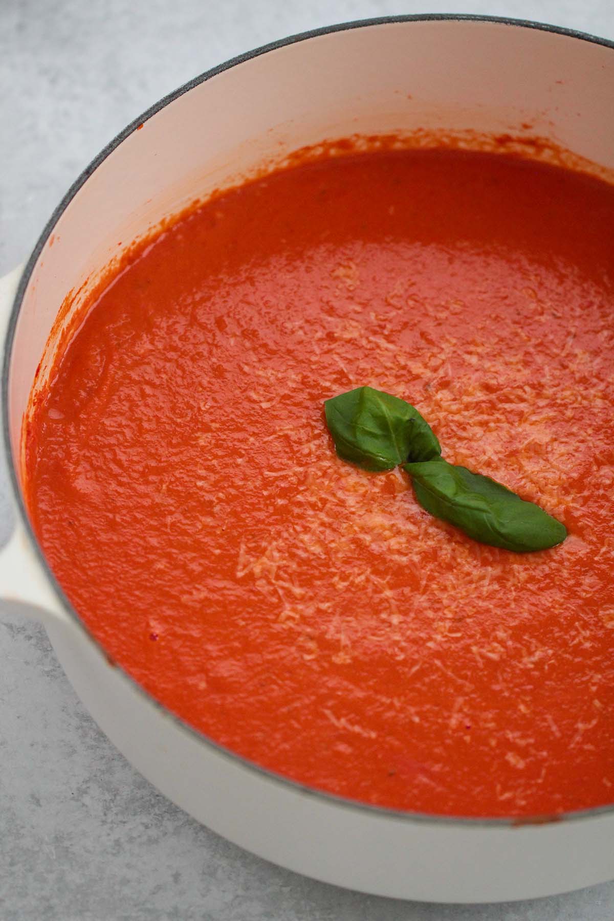 creamy tomato soup with fresh basil  in a large white pot. 