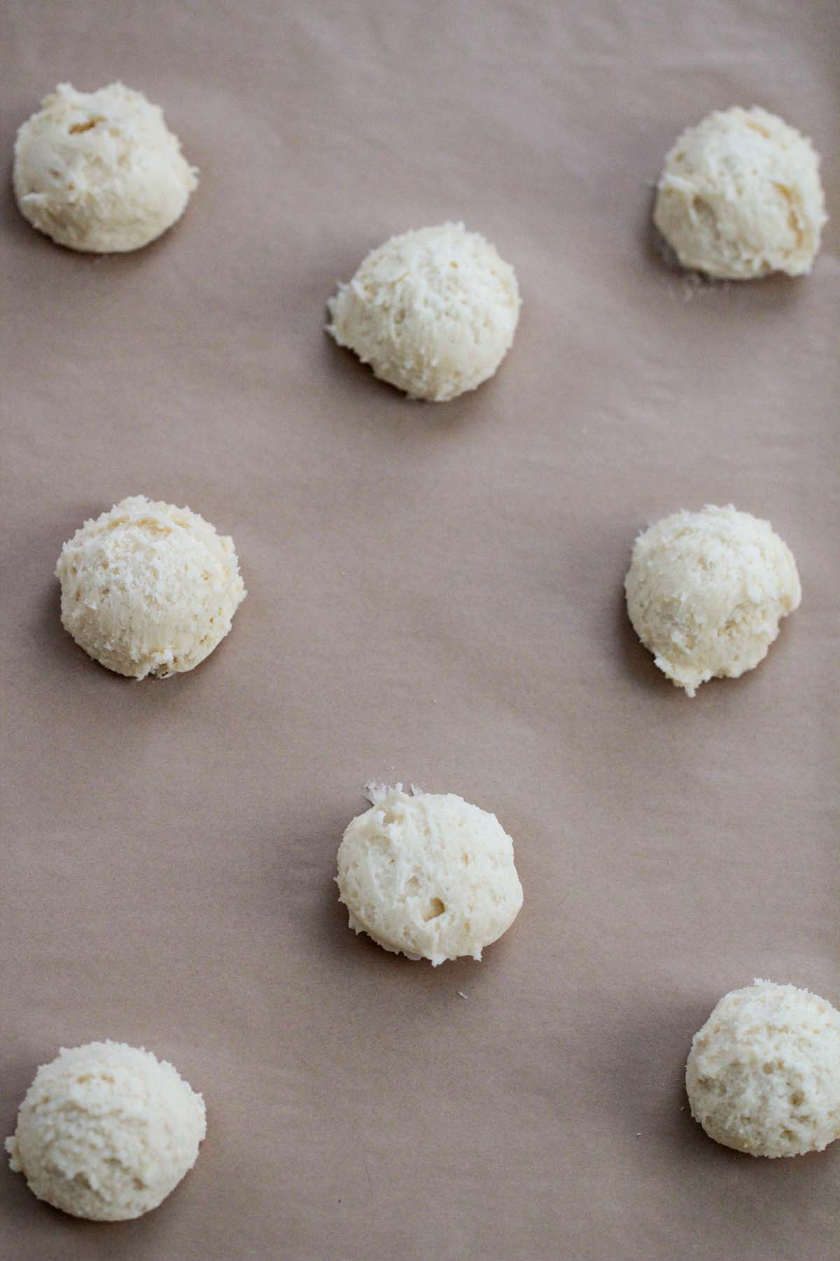 eight cookie dough balls on a baking sheet.
