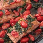 salmon with tomatoes and spinach in a skillet.