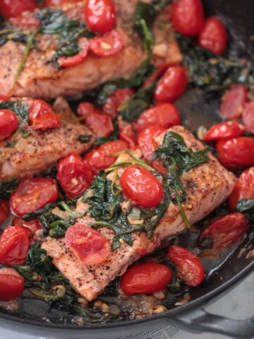 salmon with tomatoes and spinach in a skillet.