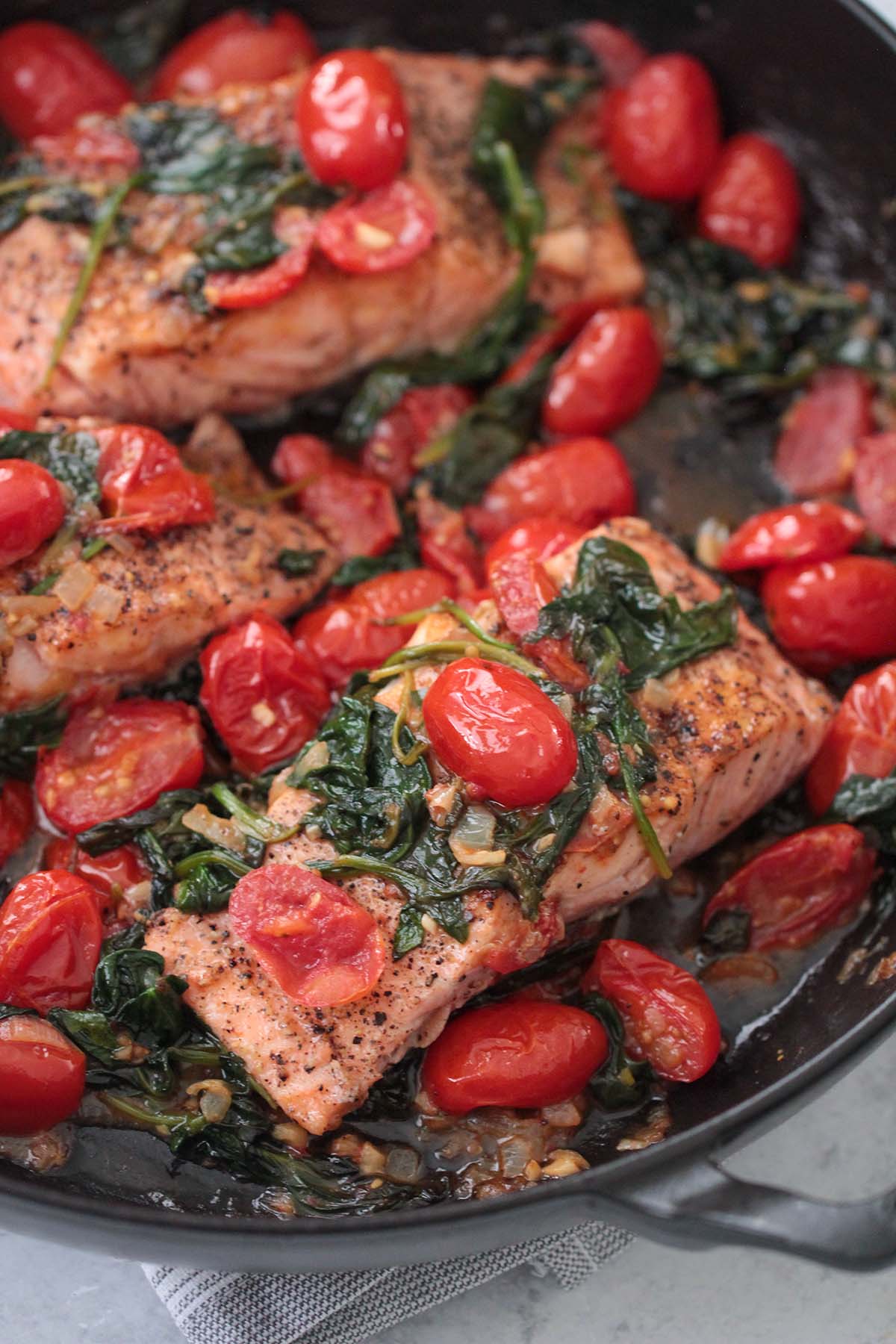 salmon with tomatoes and spinach in a skillet. 
