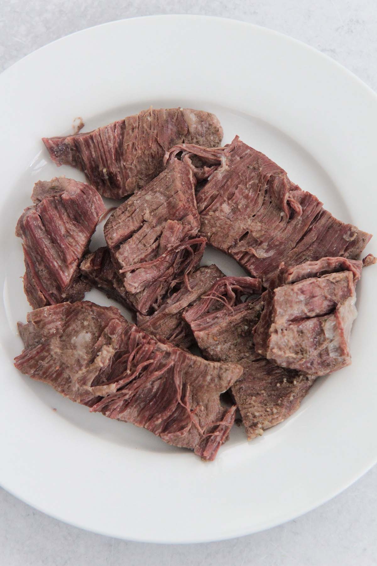 shredded flank steak on a white plate. 