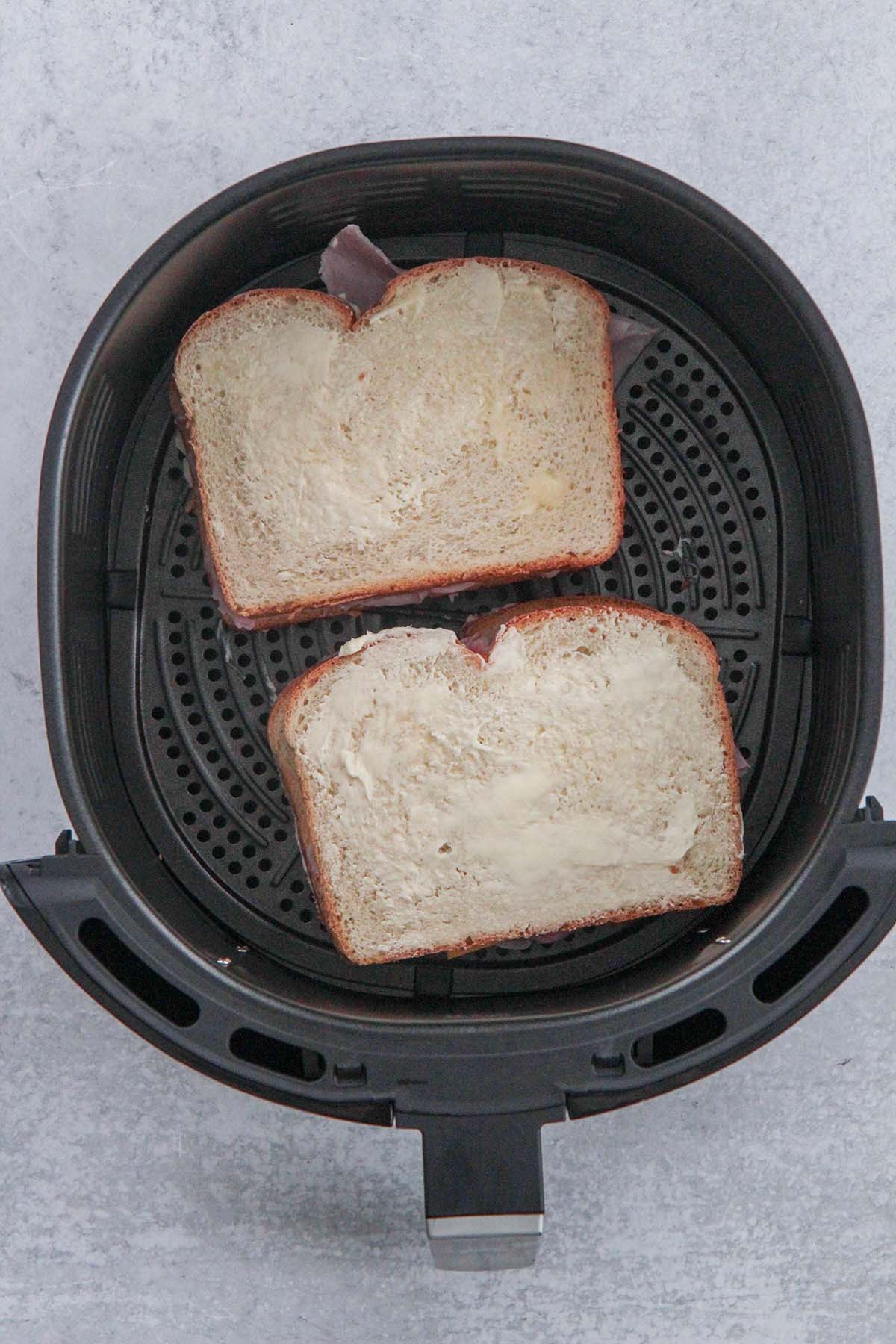 two ham and cheese sandwiches in the air fryer basket. 