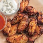 air fryer chicken wings on a plate with buffalo sauce and blue cheese dressing on the side.