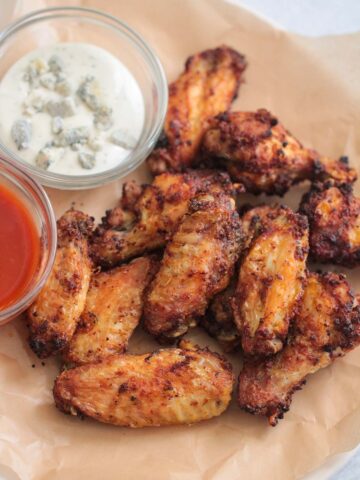 air fryer chicken wings on a plate with buffalo sauce and blue cheese dressing on the side.