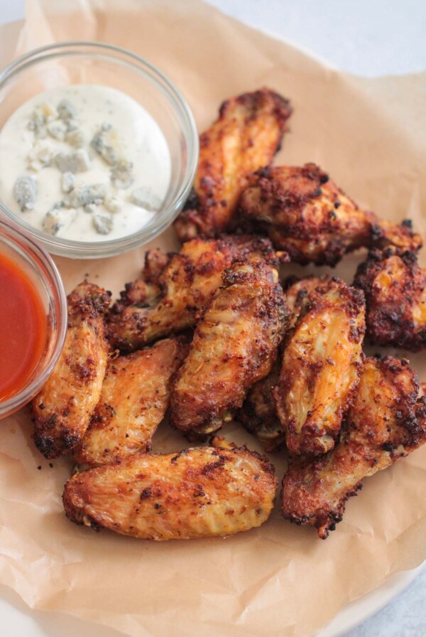 air fryer chicken wings on a plate with buffalo sauce and blue cheese dressing on the side.
