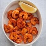 air fryer honey chipotle shrimp in a a white dish with a lemon wedge on the side.