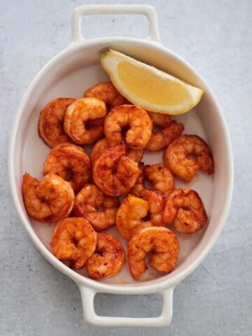 air fryer honey chipotle shrimp in a a white dish with a lemon wedge on the side.