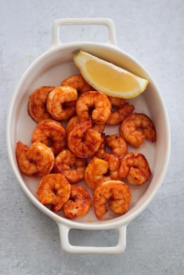 air fryer honey chipotle shrimp in a a white dish with a lemon wedge on the side.