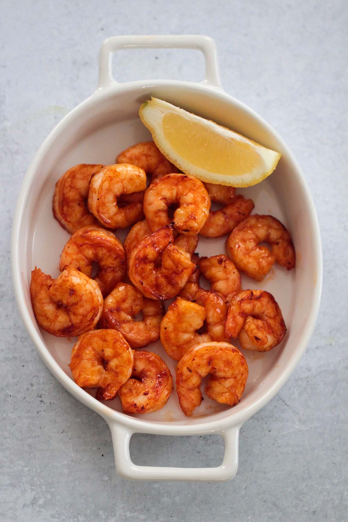 air fryer honey chipotle shrimp in a a white dish with a lemon wedge on the side. 