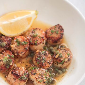 lemon butter scallops on a white plate with a lemon wedge on the side.