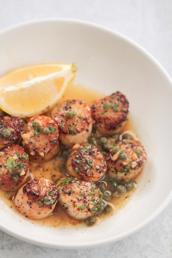 lemon butter scallops on a white plate with a lemon wedge on the side.