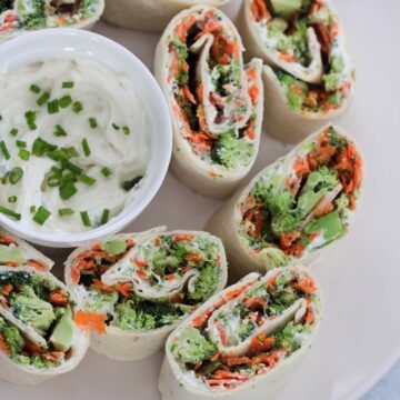 veggie cream cheese roll-ups on a plate with a small bowl of cream cheese mixture.