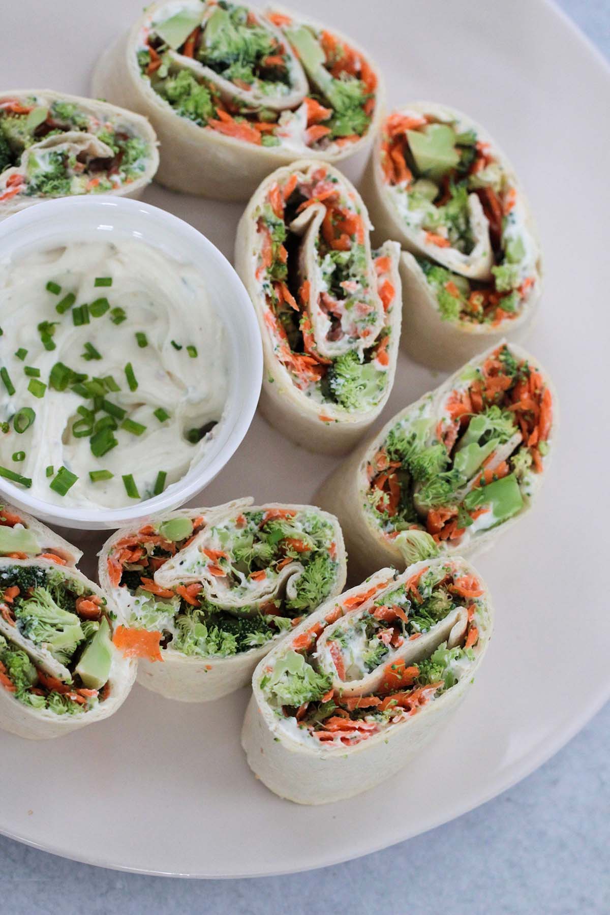 veggie cream cheese roll-ups on a plate with a small bowl of cream cheese mixture. 