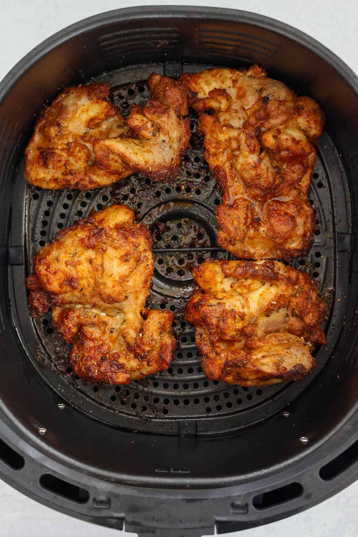 Four cooked boneless chicken thighs in the air fryer basket. 