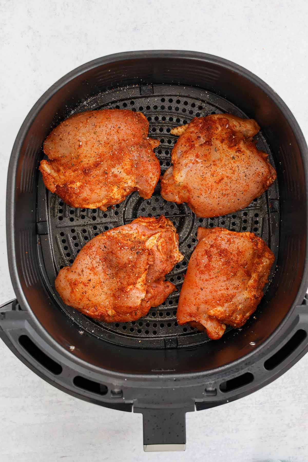 four raw seasoned chicken thighs in the air fryer basket. 