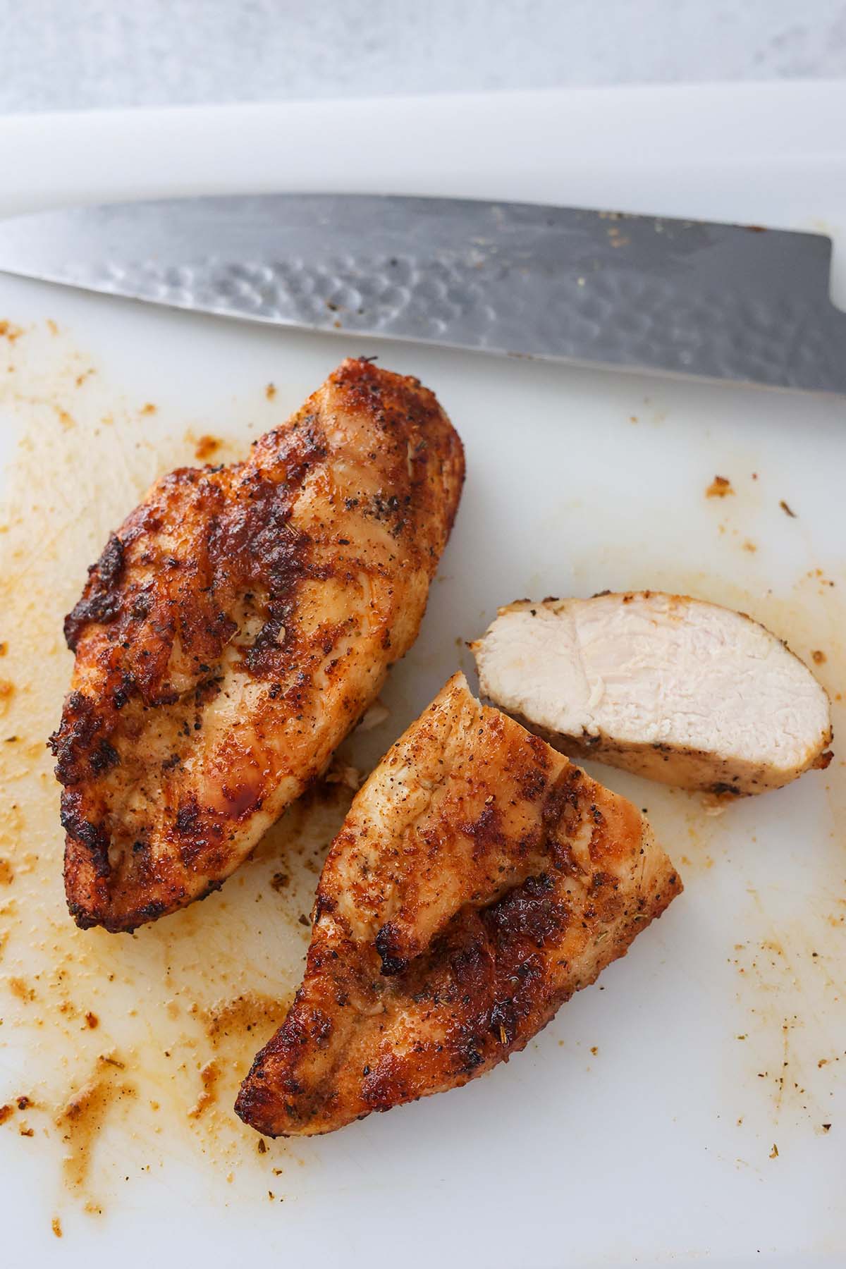 two cooked and sliced chicken breasts on a cutting board with a knife. 