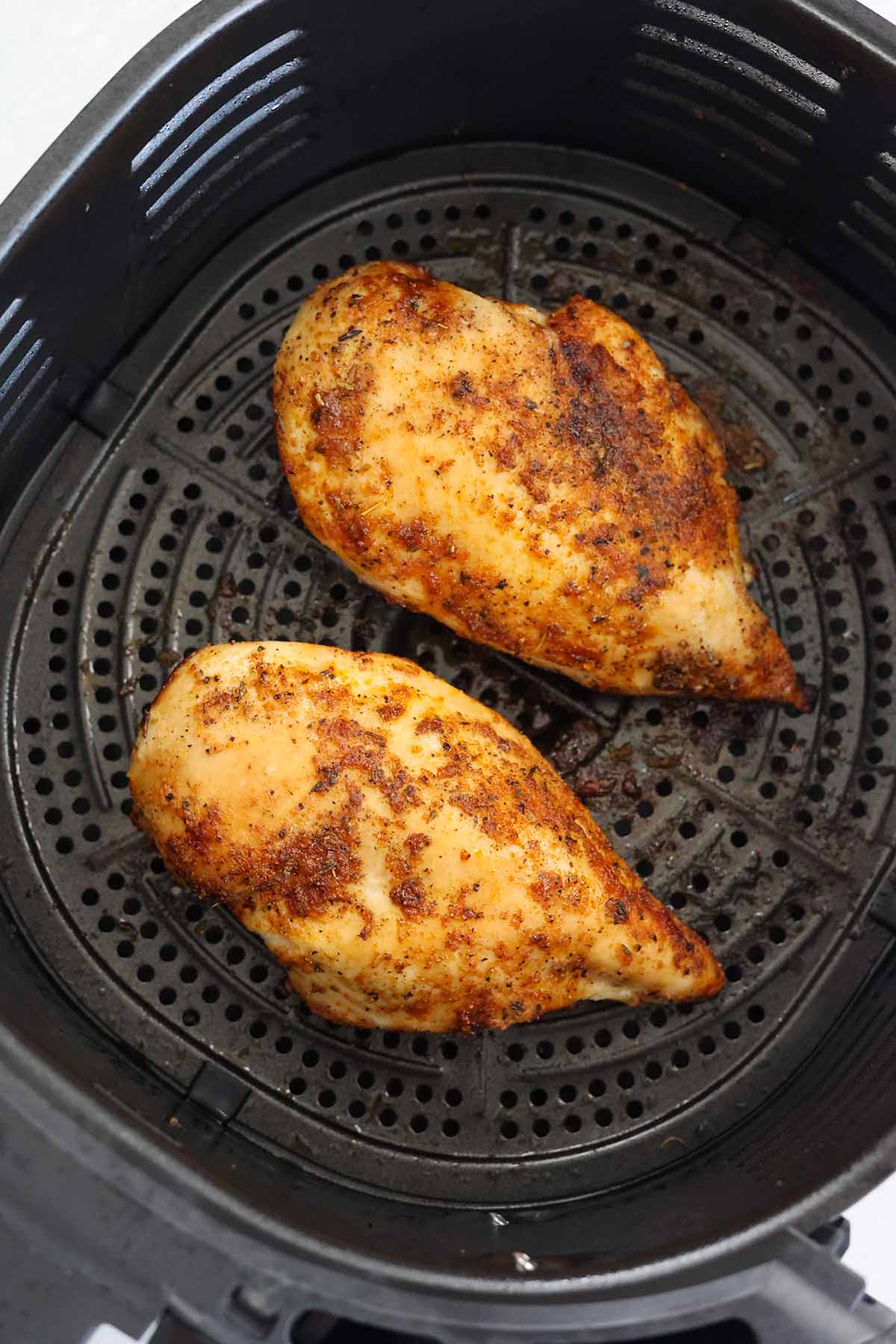 two cooked chicken breasts in the air fryer basket. 