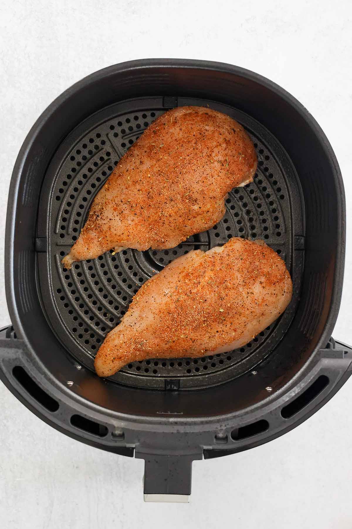 two raw chicken breasts in an air fryer basket. 