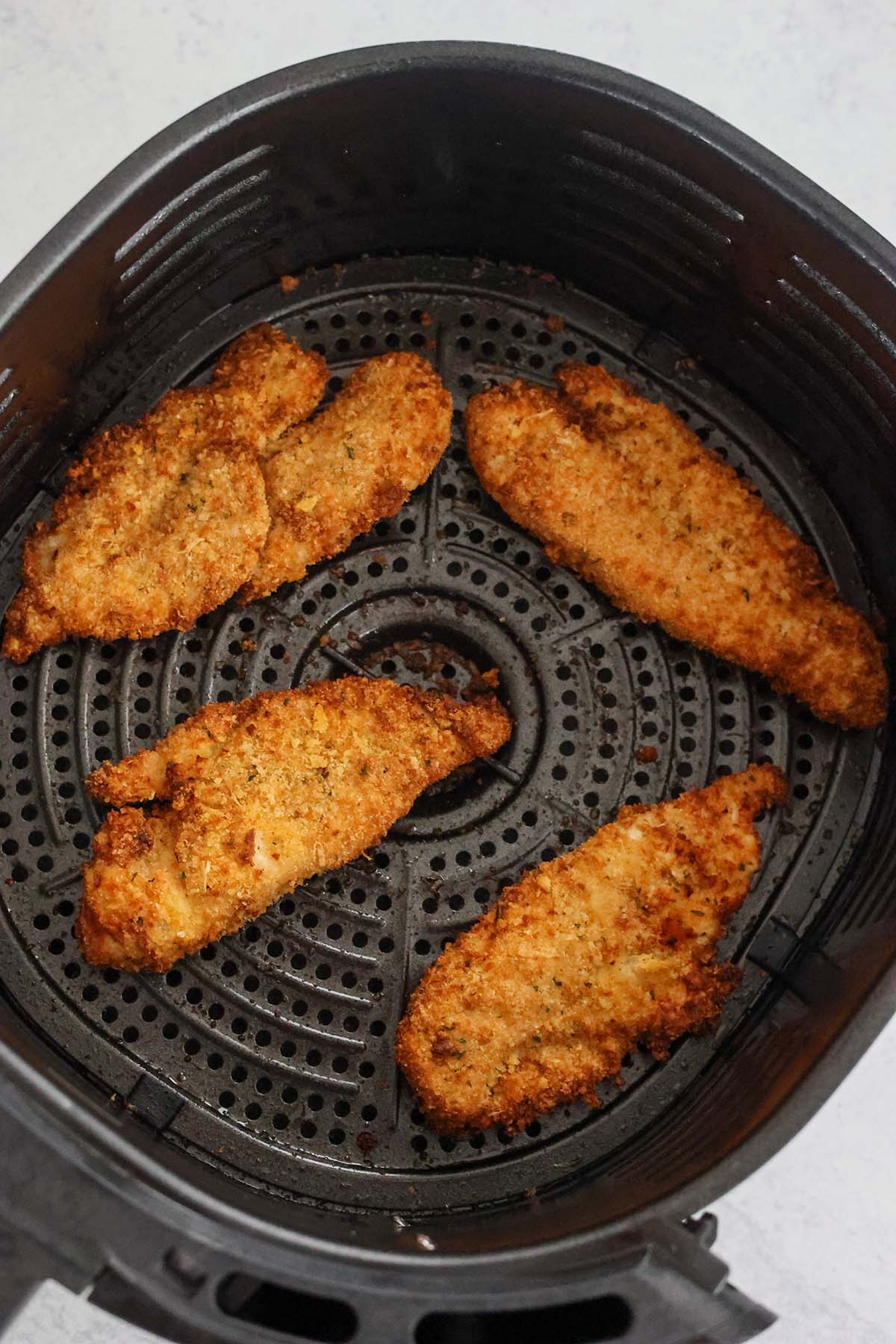 four cooked chicken tenders in the air fryer basket. 