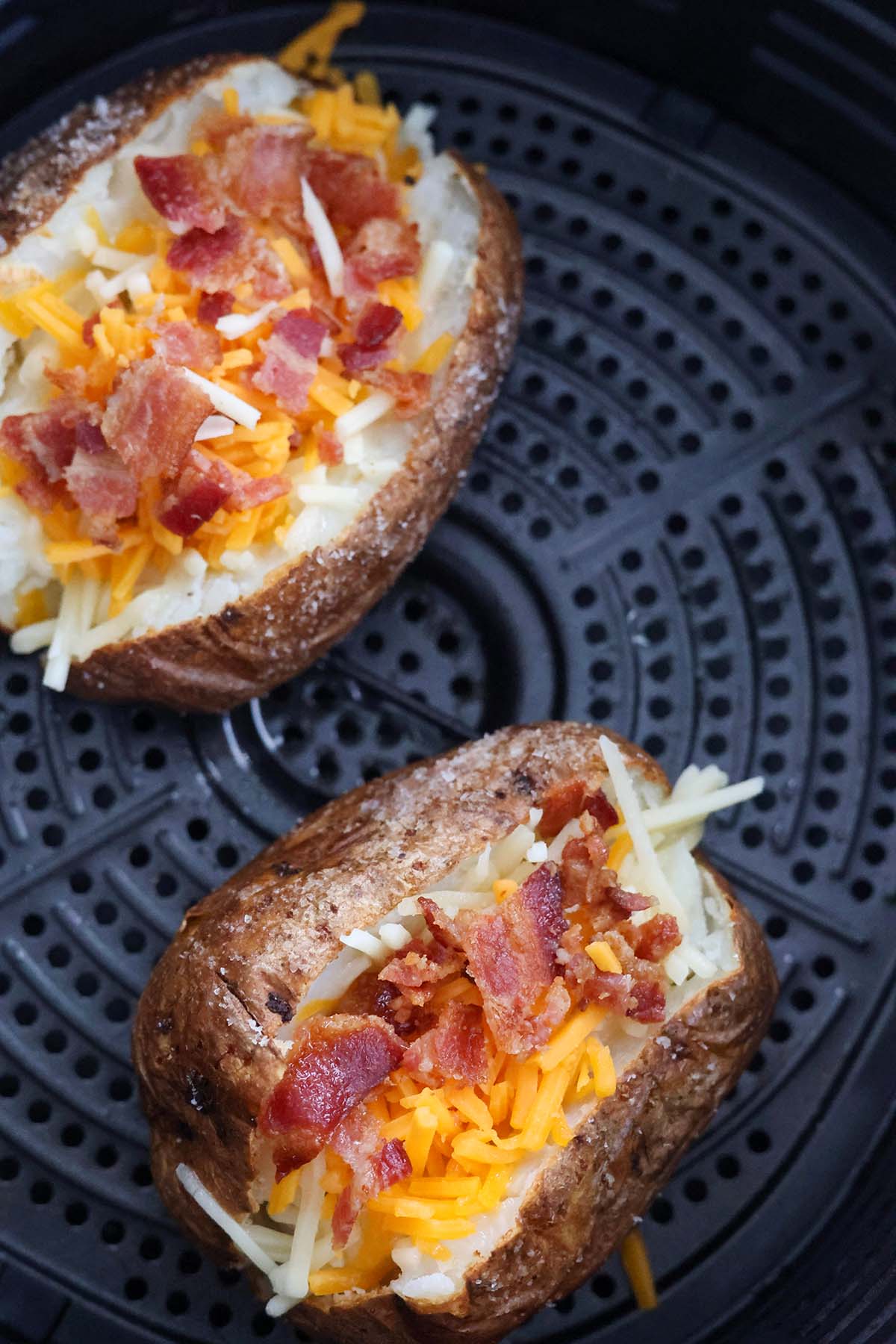 two potatoes with shredded cheese and bacon in an air fryer. 