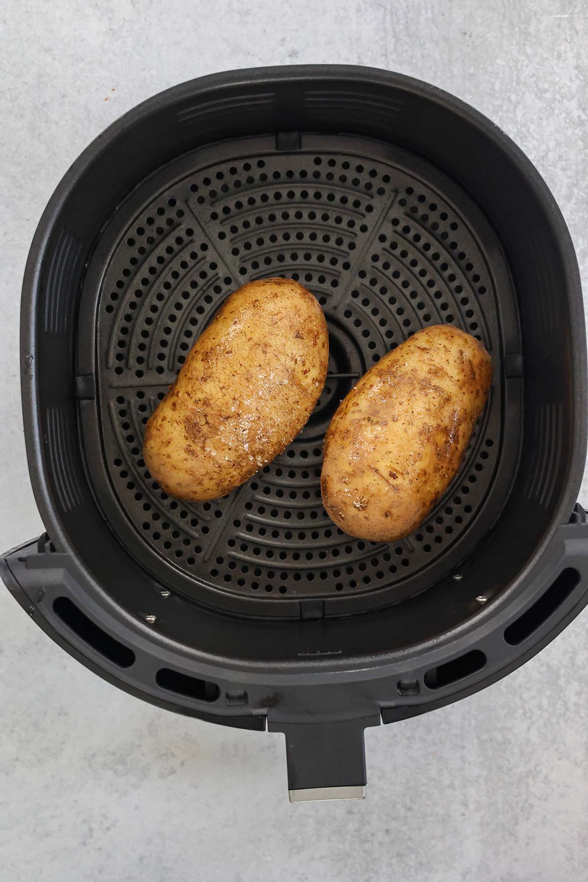 two russet potatoes in the air fryer basket. 