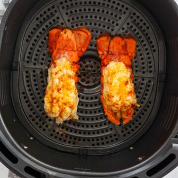 two cooked lobster tails in the air fryer basket.