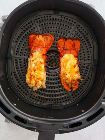 two cooked lobster tails in the air fryer basket.