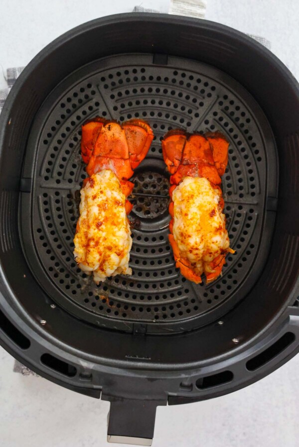 two cooked lobster tails in the air fryer basket.