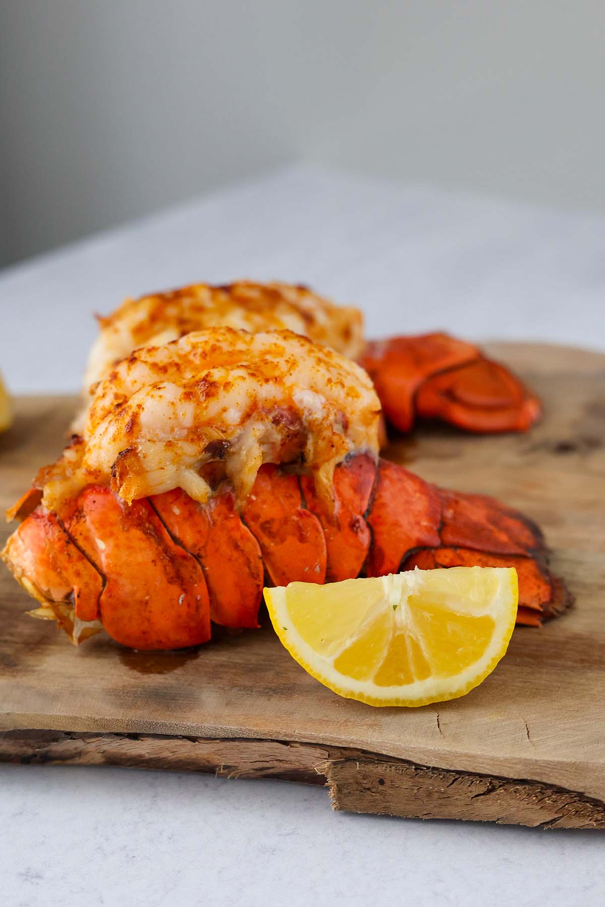 two cooked lobster tails on a cutting board with a lemon wedge on the side. 