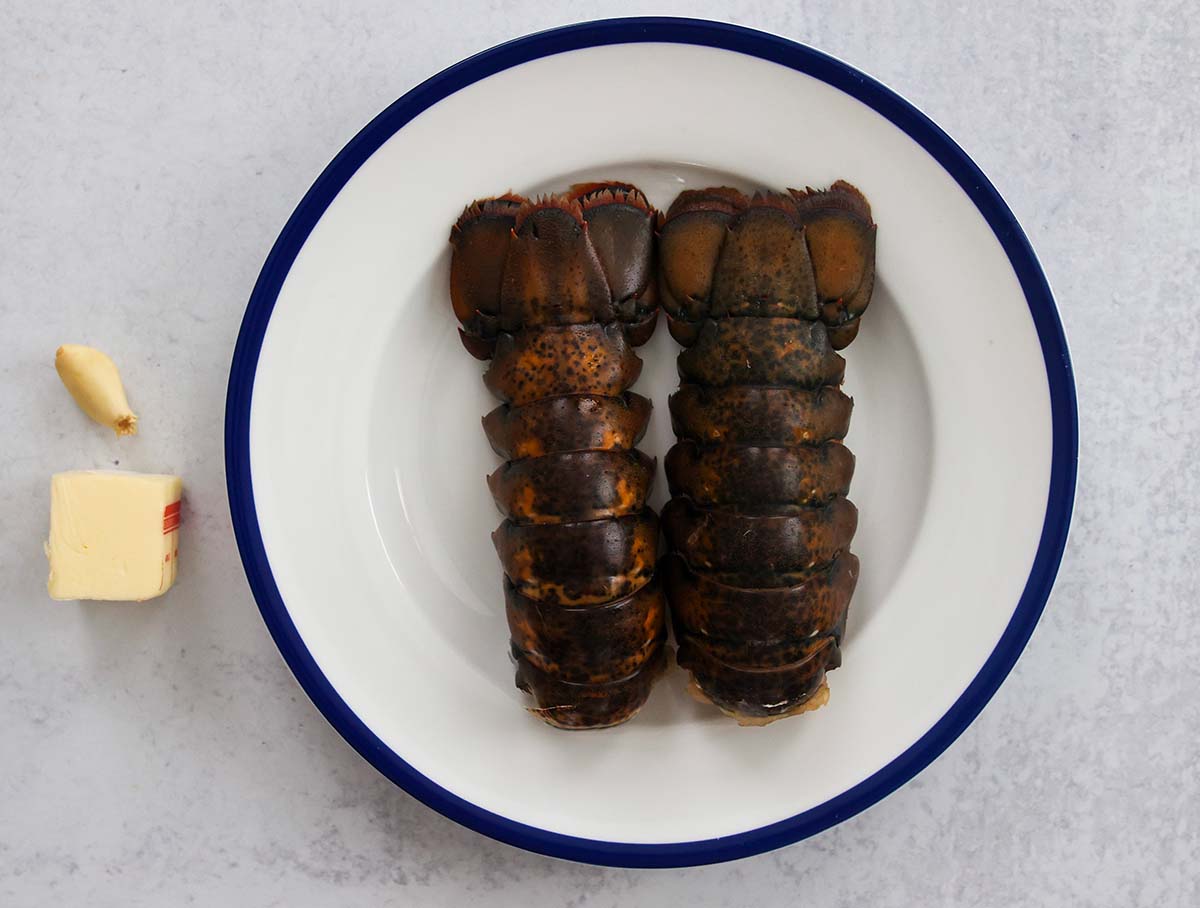 two raw lobster tails with butter and a garlic clove on the side. 