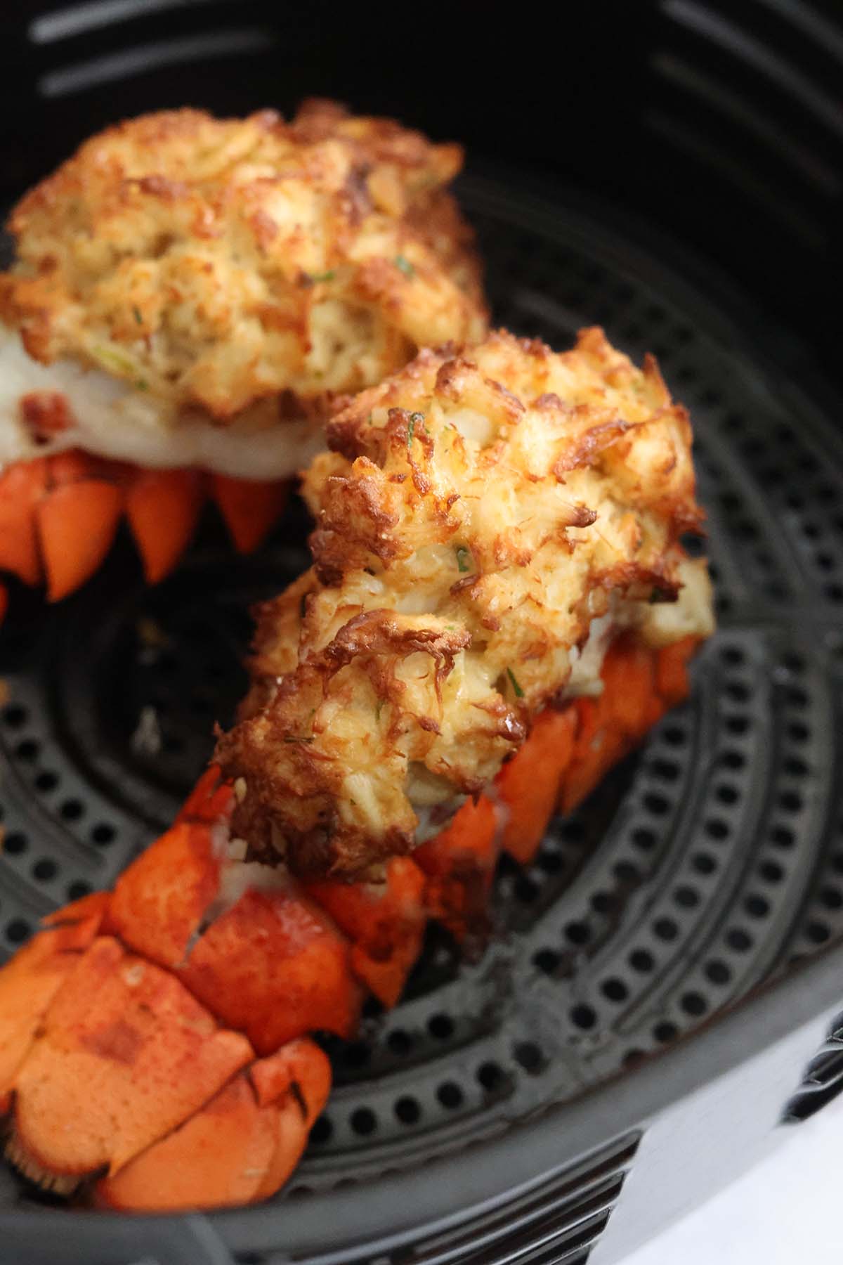 two cooked stuffed lobster tails in the air fryer basket.