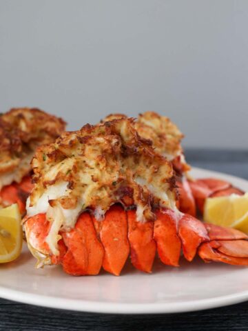 air fryer stuffed lobster tails on a plate with lemon wedges.