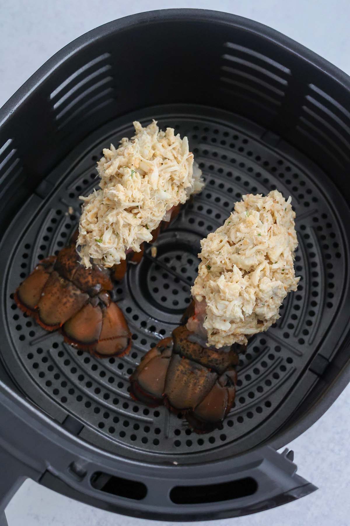 two raw stuffed lobster tails in the air fryer basket.