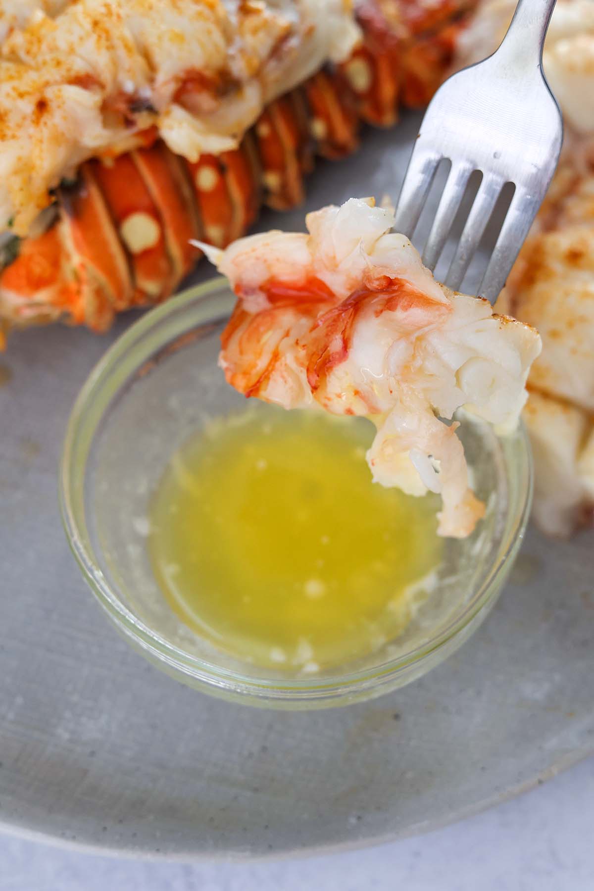 A fork dipping cooked lobster meat into melted butter. 