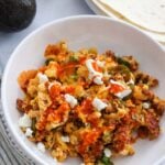 chorizo scrambled eggs with cheese and hot sauce on top.