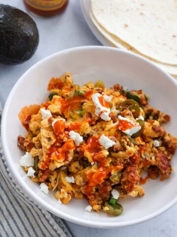 chorizo scrambled eggs with cheese and hot sauce on top.