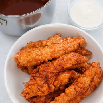 hot honey chicken tenders on a white plate with sauces on the side.