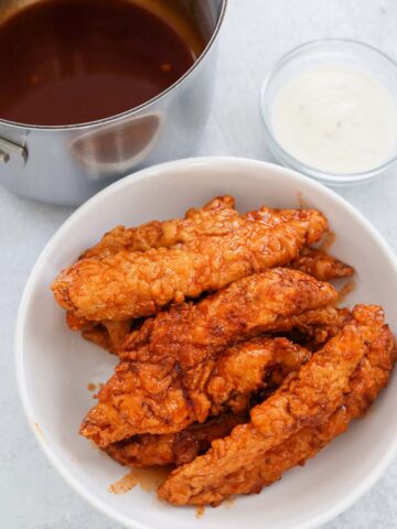 hot honey chicken tenders on a white plate with sauces on the side.
